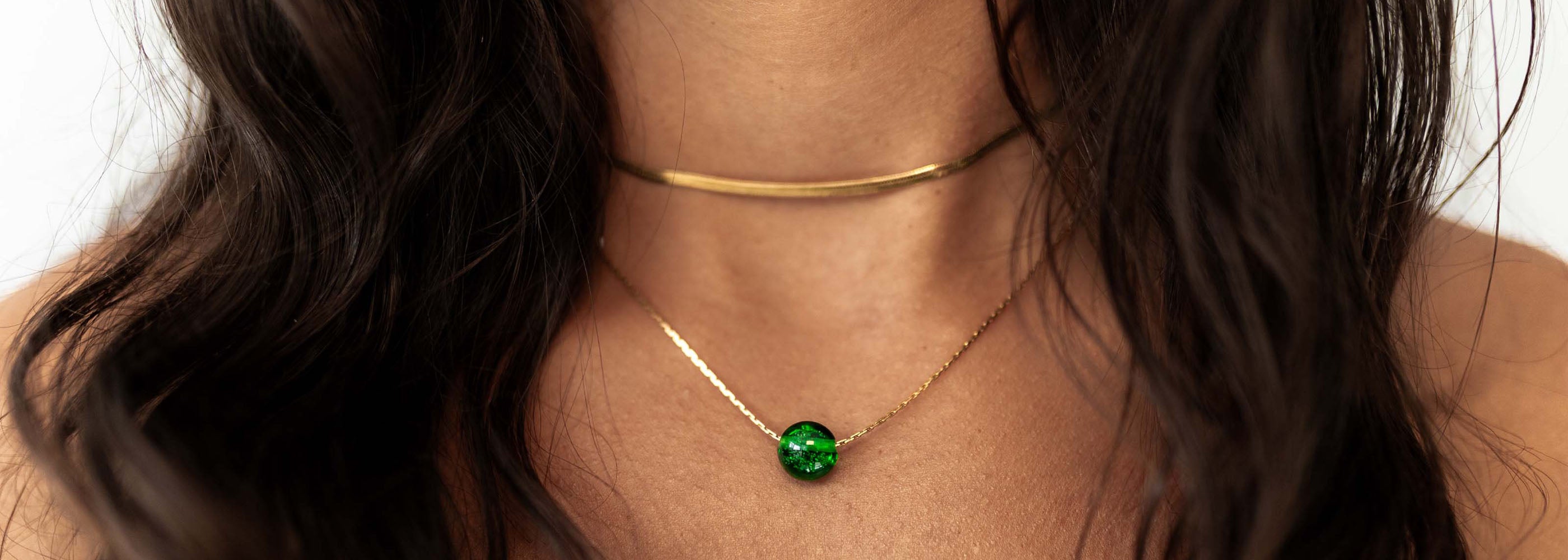 Dark haired woman wearing gold necklaces and a green glass sand pebble.