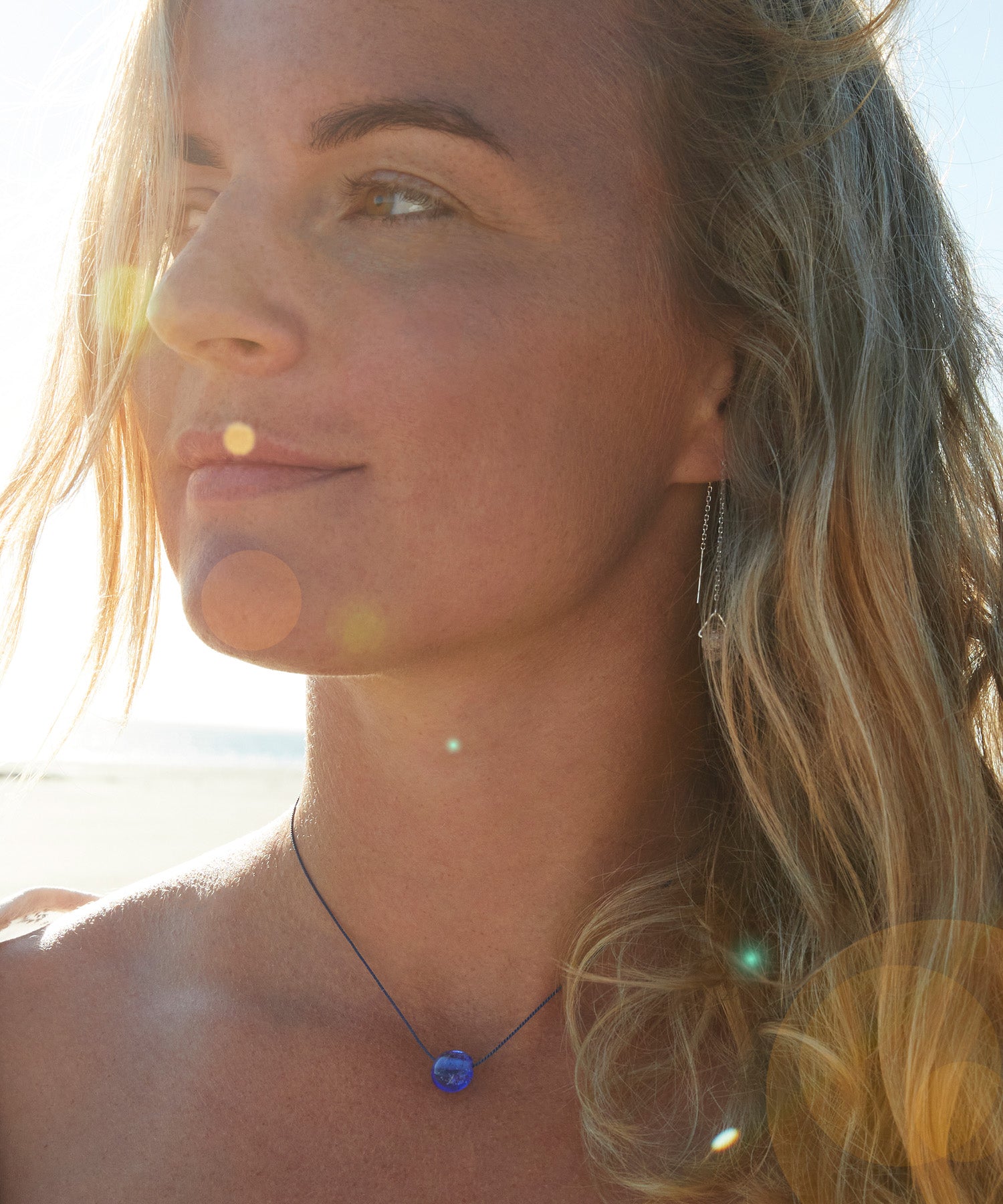 Woman on beach wearing blue sand jewellery necklace.