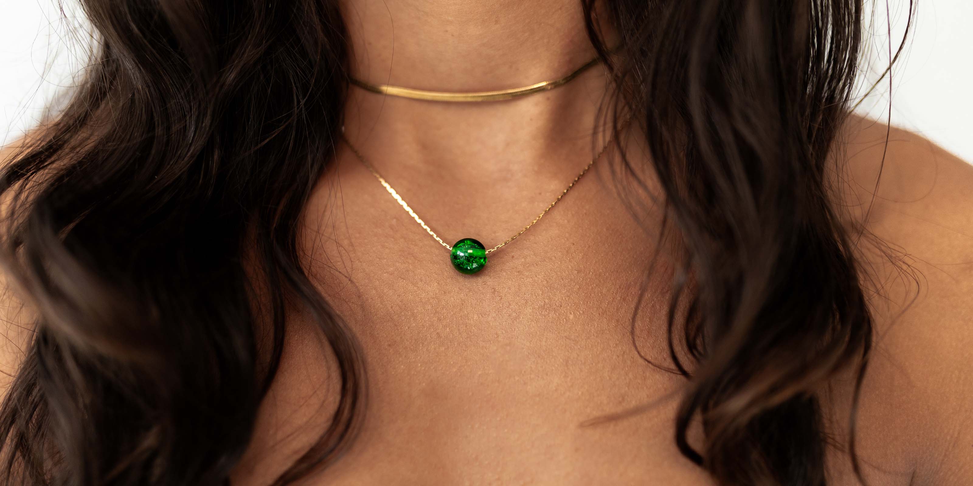 Dark haired woman wearing gold necklaces with green glass bead.