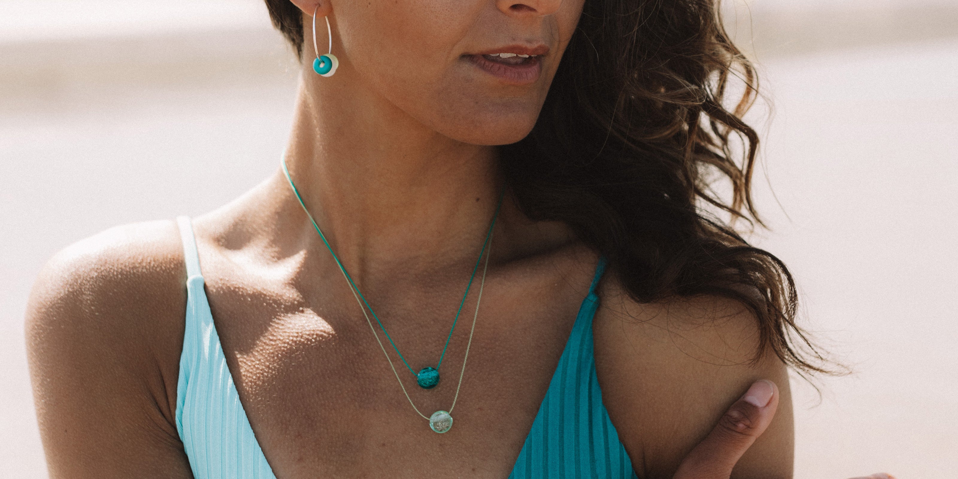Dark haired girl on the beach wearing layered necklaces in teal and green fine cord.