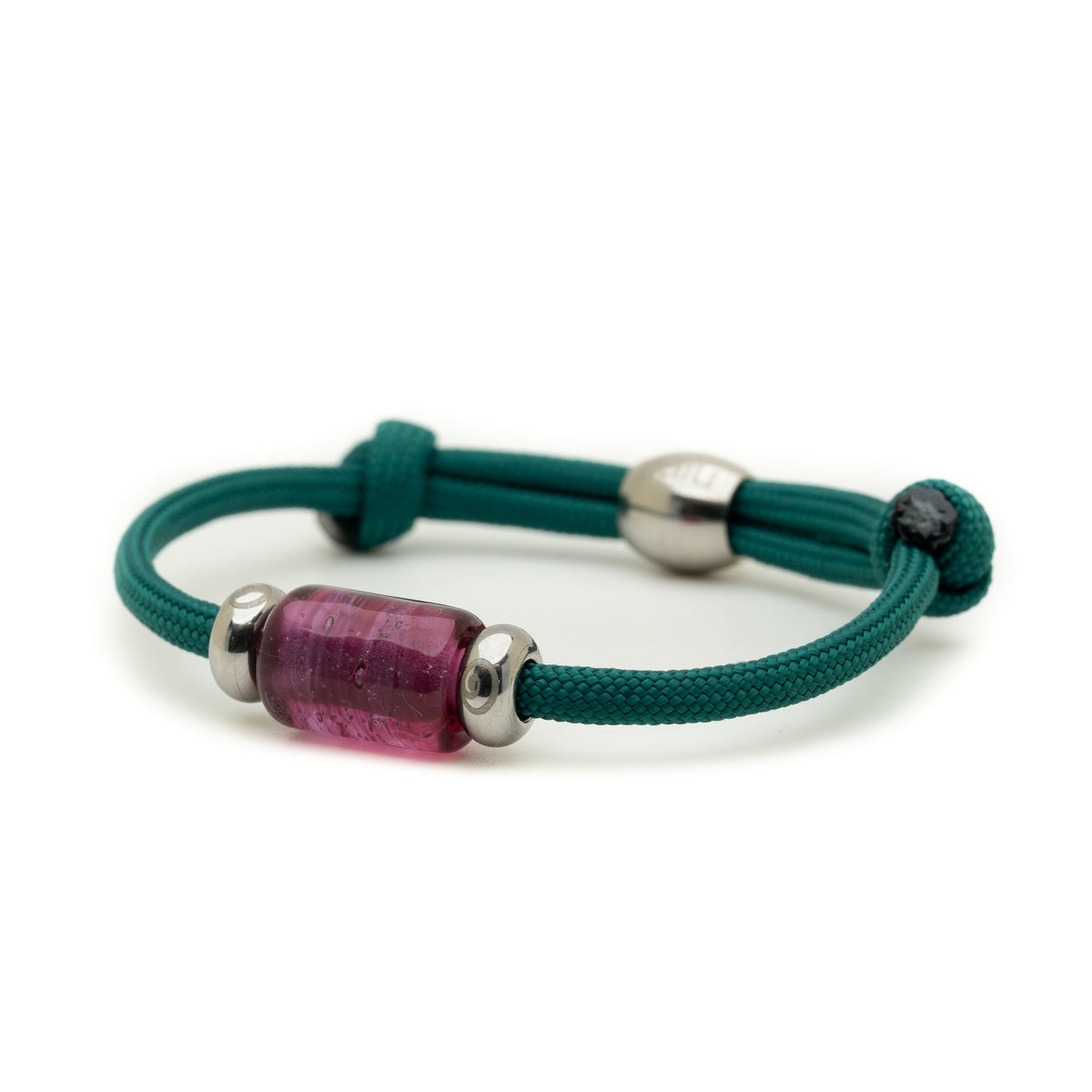 A dark teal green cord bracelet featuring a central translucent pinkish-purple cylindrical bead flanked by two polished silver metal spacers, shown on a clean white background.