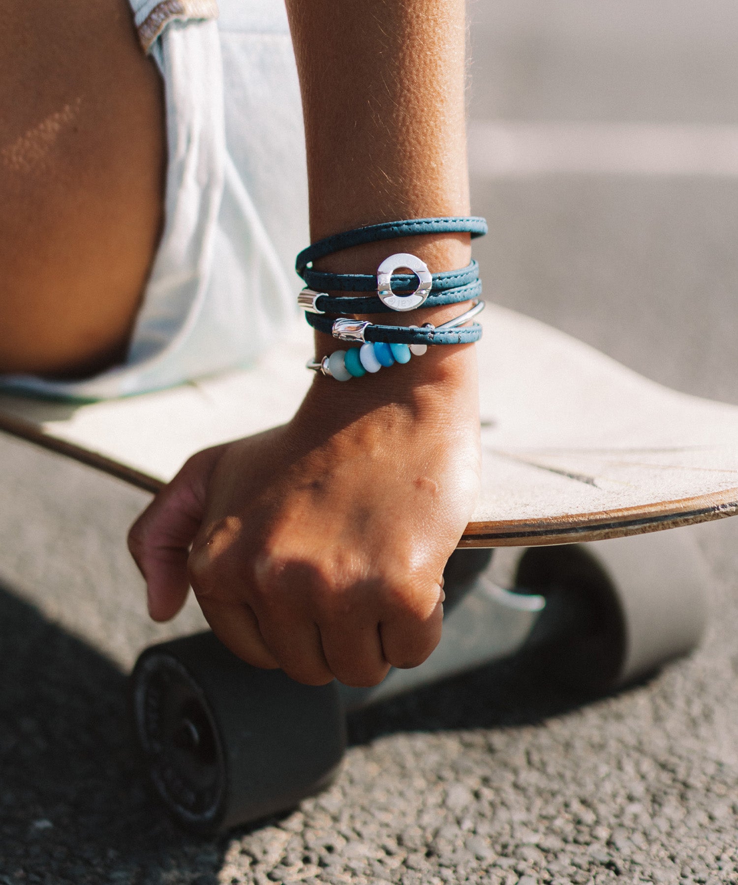 Person on skateboard wearing cork bracelet with silver charms and a beaded bangle.