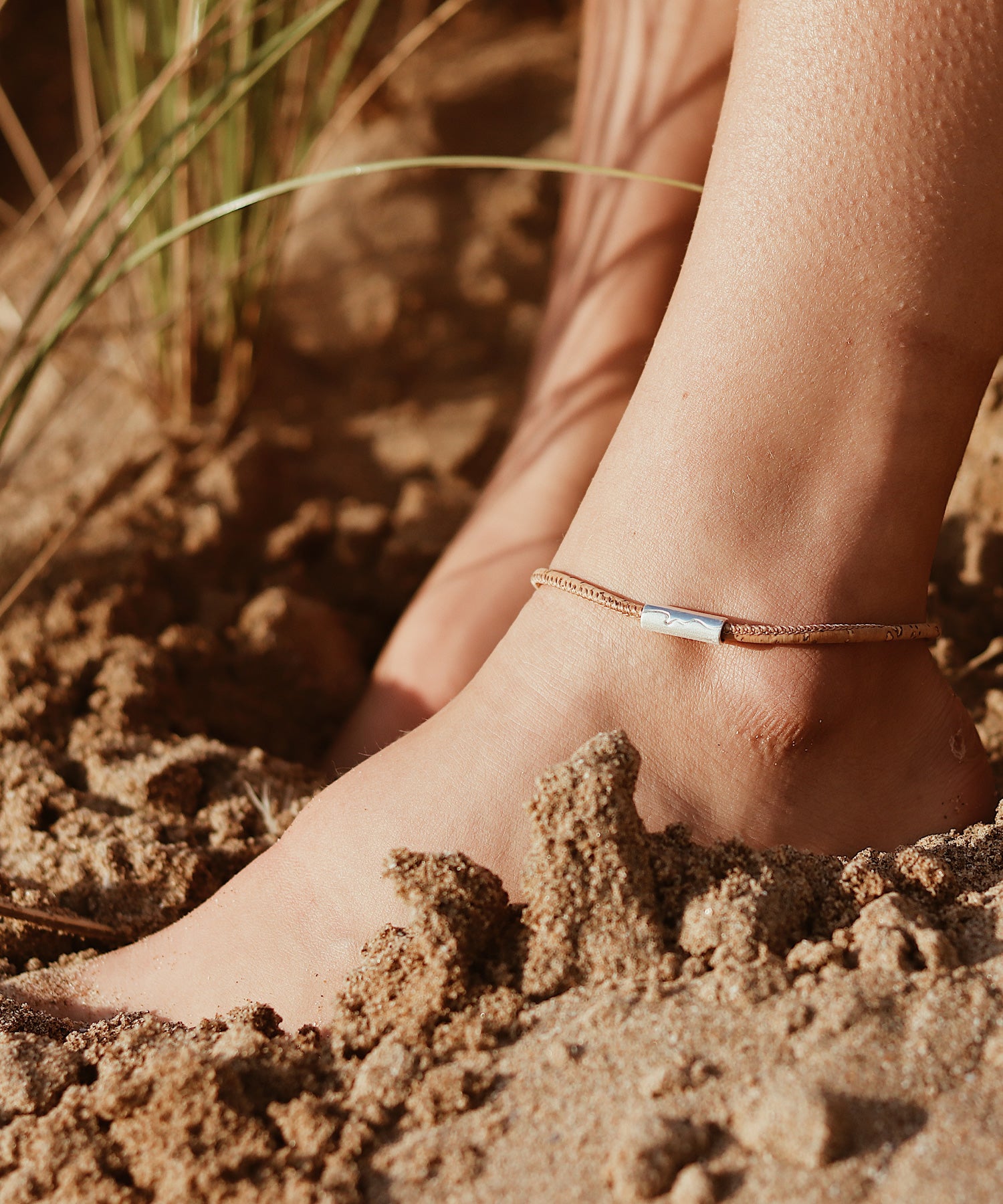 Silver north Devon coastline bead worn on leather anklet but girl on beach with feet in the sand.