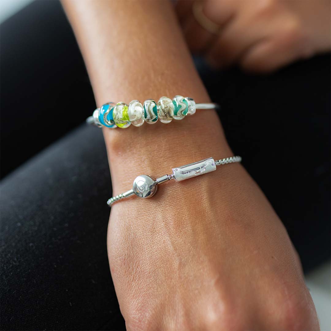 Person wearing a beaded bangle and a silver bracelet with tube charm.