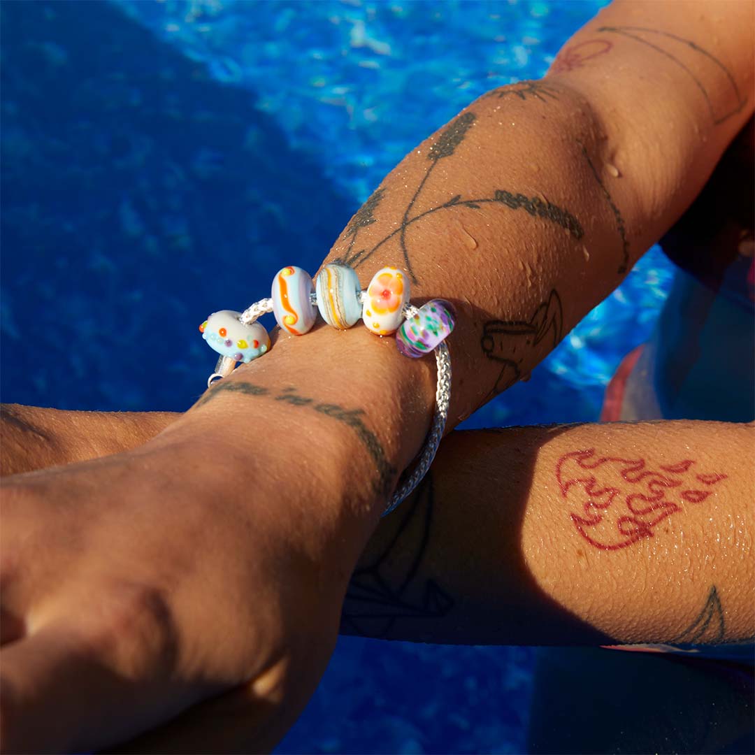 Person in a swimming pool with arms folded wearing a chunky silver bracelet with coloured Murano glass beads.