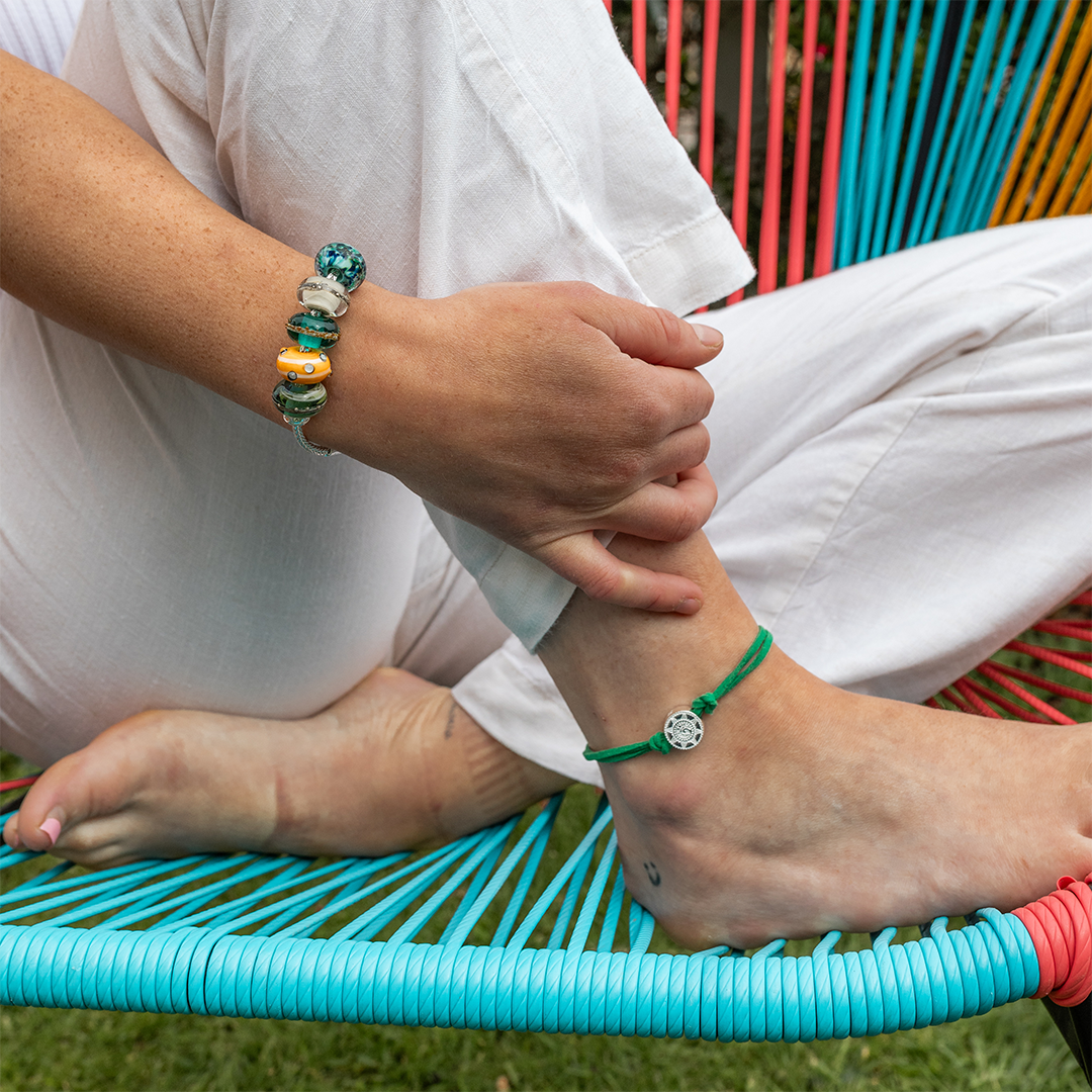 Person sitting in a deck chair wearing a colourful beaded bracelet and green cork anklet with silver charm.