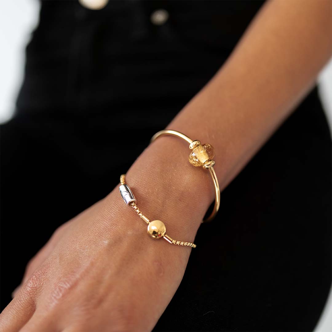 Person wearing gold hula bracelet and gold bangle with glass bead.