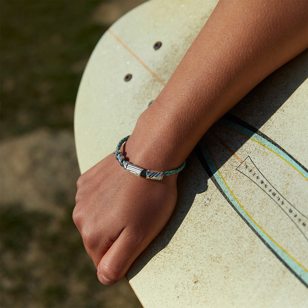 Person carrying skateboard with a leather blue bracelet and silver beads.