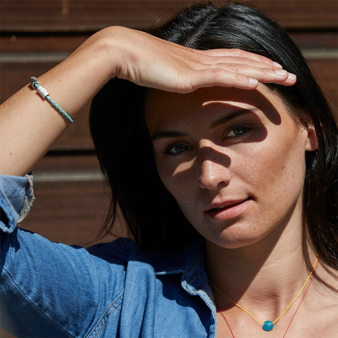 Dark haired woman in denim shirt wearing necklace and bracelet.