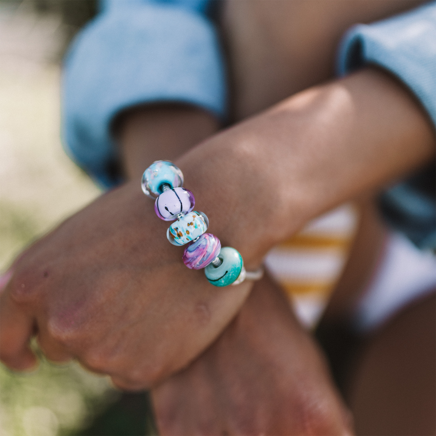 Person wearing silver bracelet with blue, purple and green coloured glass surf beads.