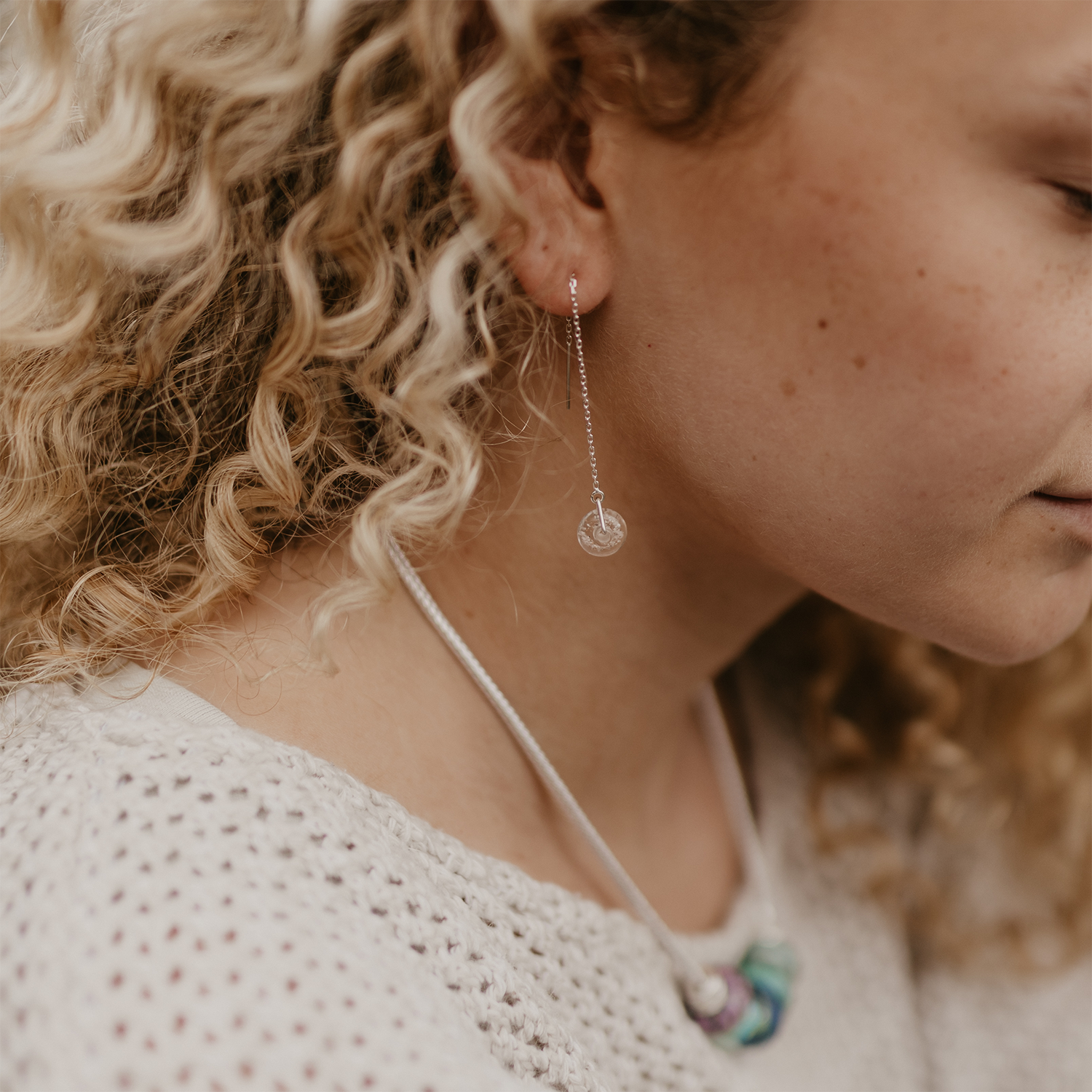 Silver thread through earrings worn by girl on the beach.