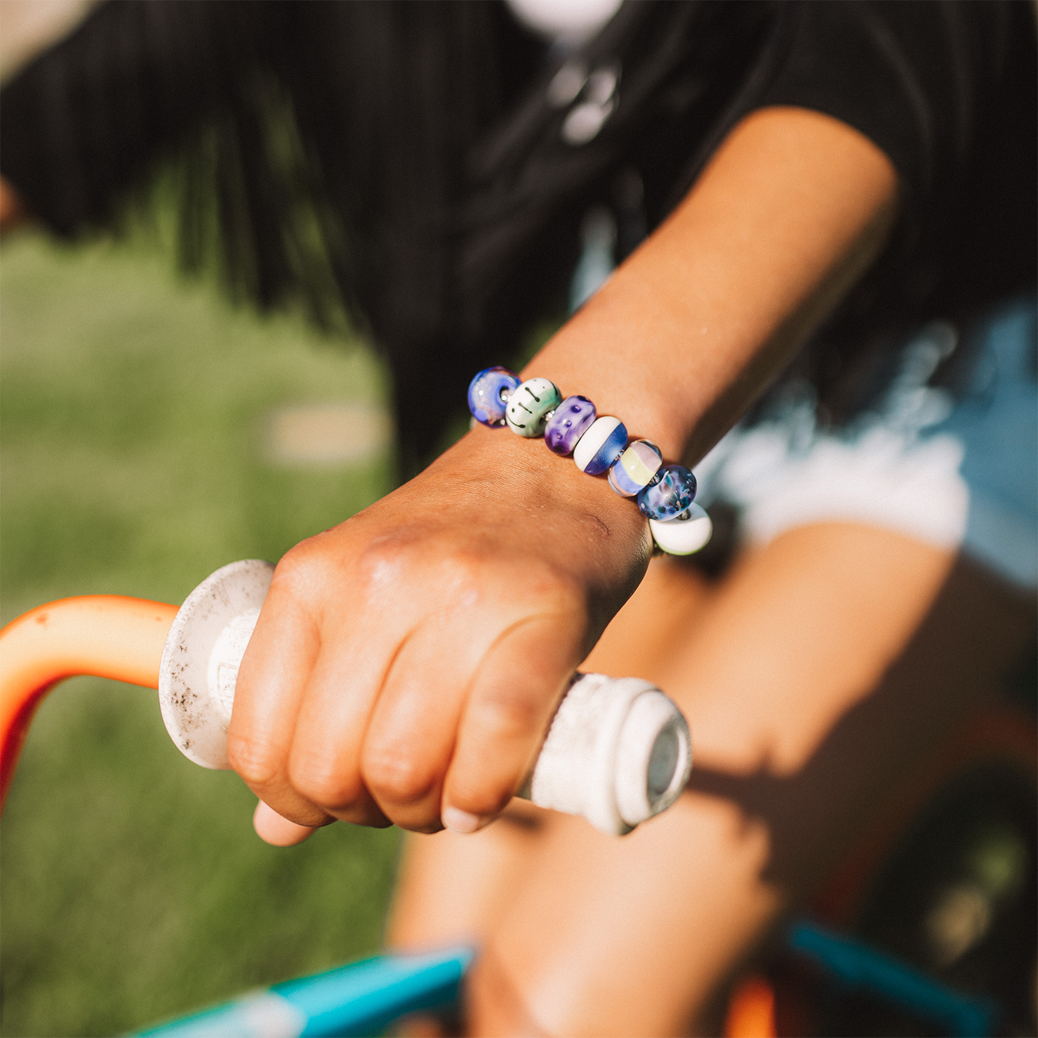 Woman on BMX bike wearing black jacket and colourful beaded bracelet.