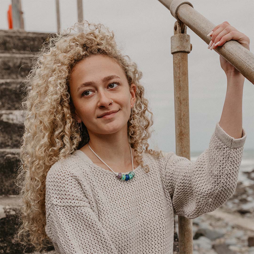 Girl on steps at seaside wearing silver chain necklace with colourful glass.