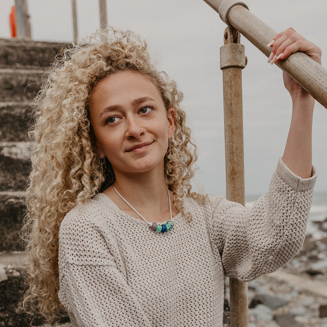 Girl sitting on harbour wearing silver necklace with UK harbour inspired beads.