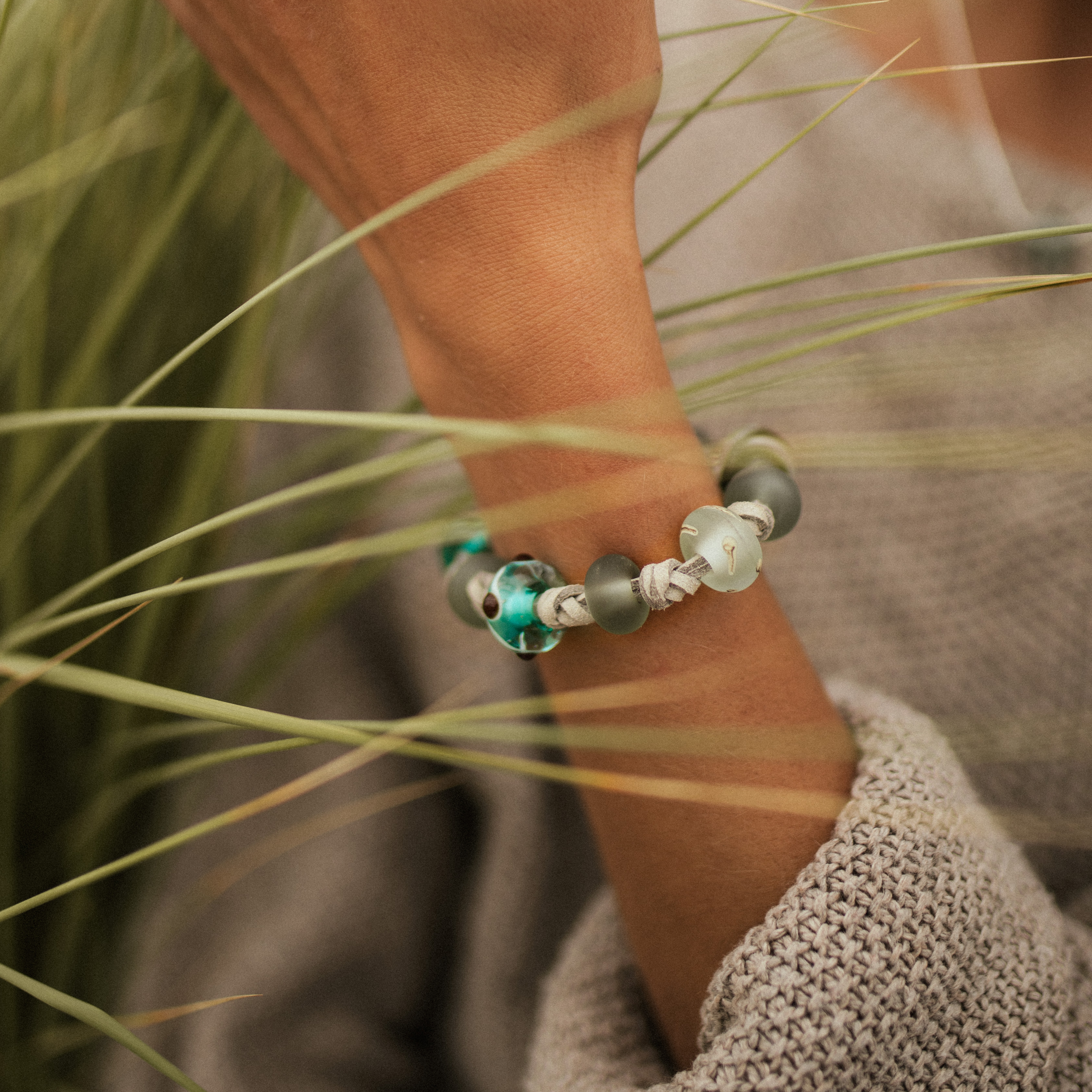 Woman wearing a grey cord bracelet with glass beads in the dune grass.