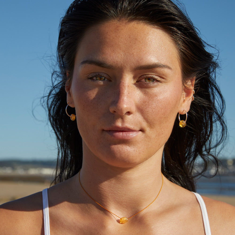 Dark hair woman wearind small silver hoop earrings with amber glass baeds and matching fine cord necklace with sand pebble, on Crow Point beach North Devon.