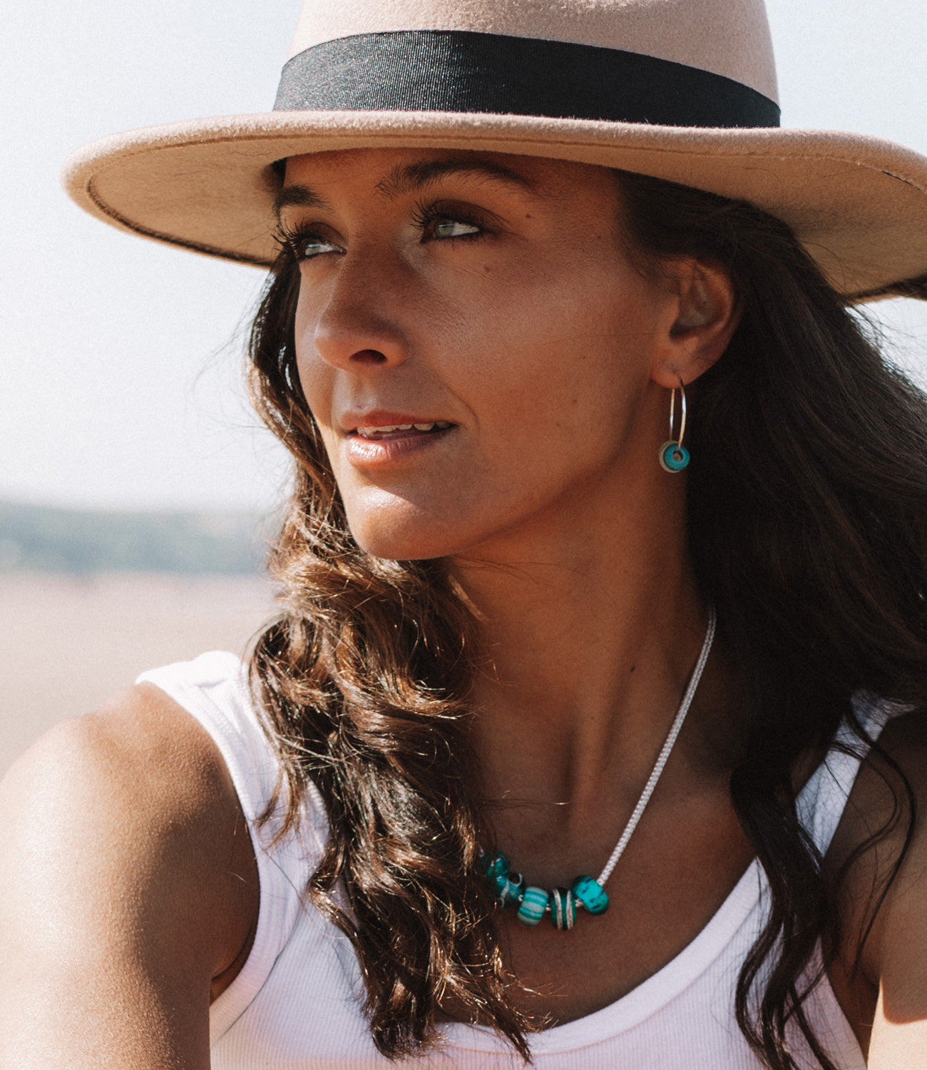 Girl on beach wearing hat and sterling silver necklace with green beads and earrings on the beach.