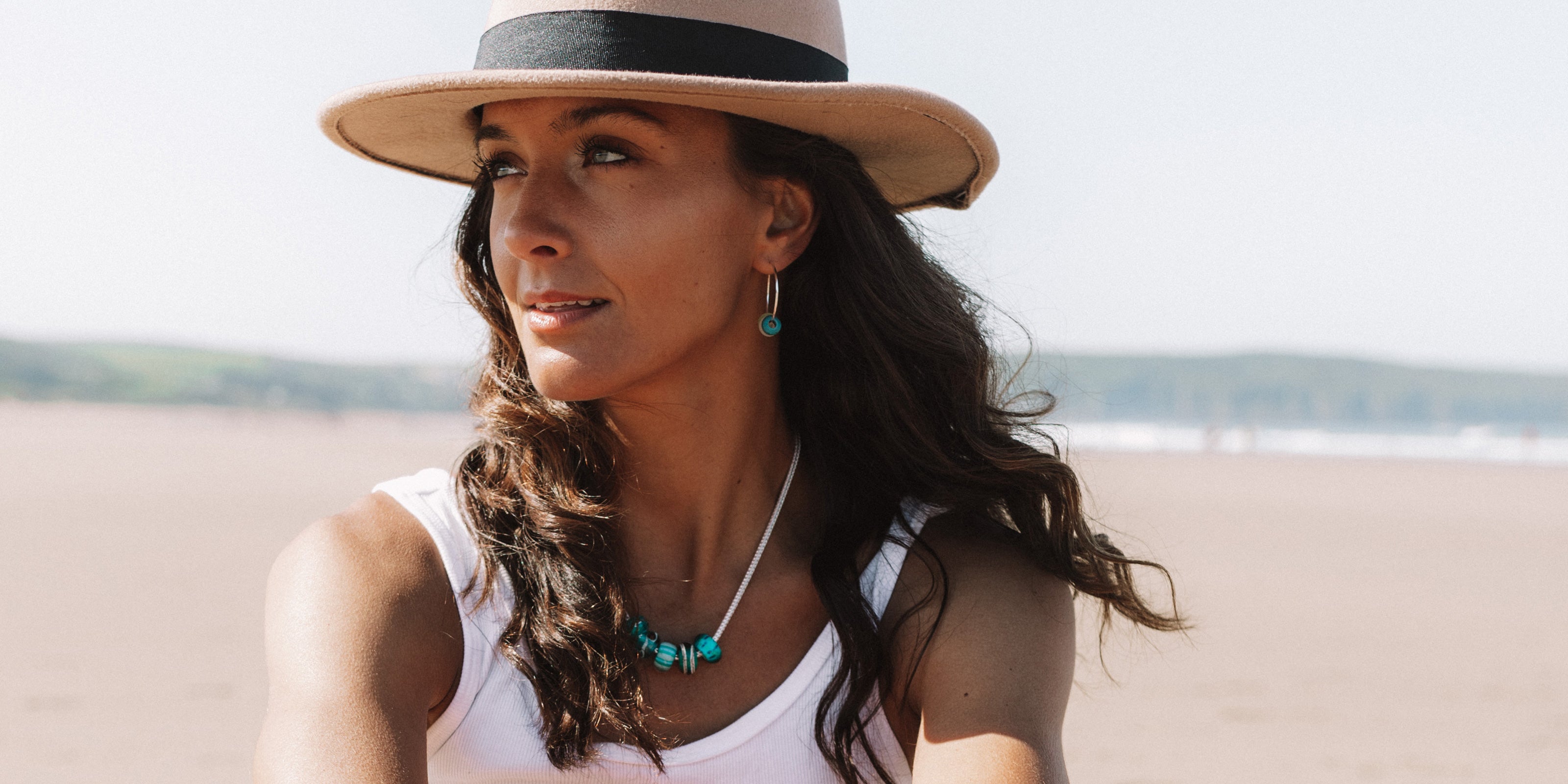 Girl on beach wearing hat and sterling silver beads and earrings on the beach.