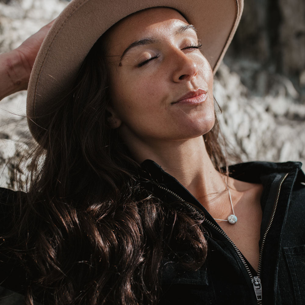 Woman wearing a beige hat and black jacket with a blurred natural background