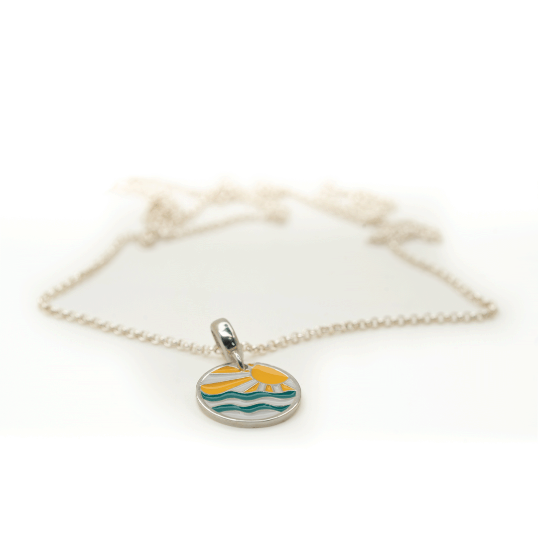 A silver chain necklace with a small round pendant featuring a yellow sun and green waves on a white background.