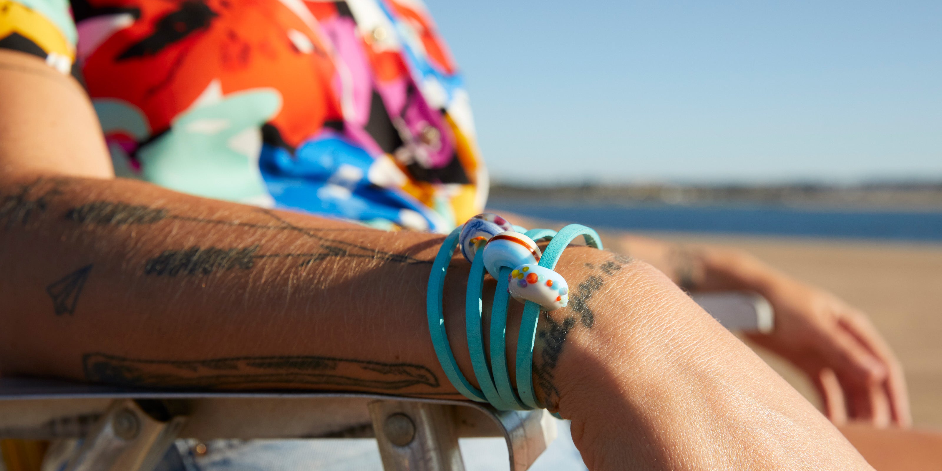 Colourful glass beads representing Sussex beaches on turquoise leather wrap bracelet, sitting on deck chair at the beach.