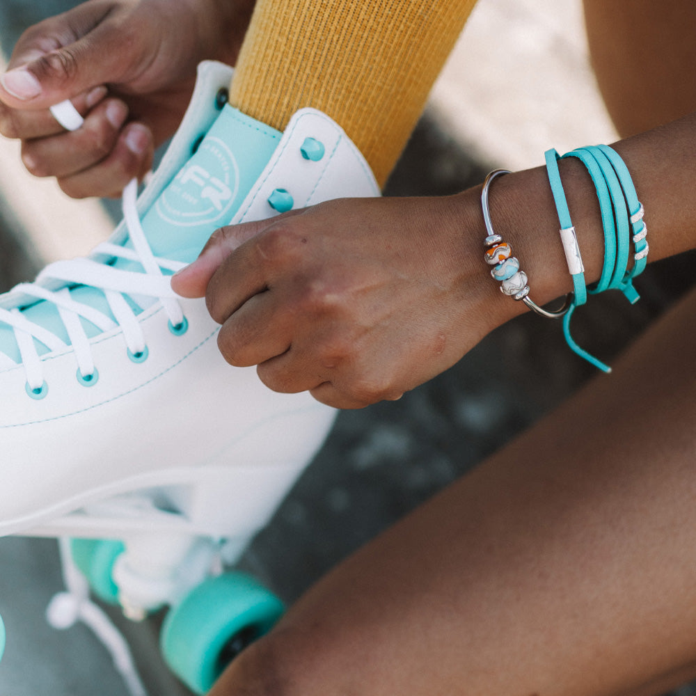 Person tying laces on their roller skates wearing a silver beaded bangle and turquoise wrap bracelet with silver charms.