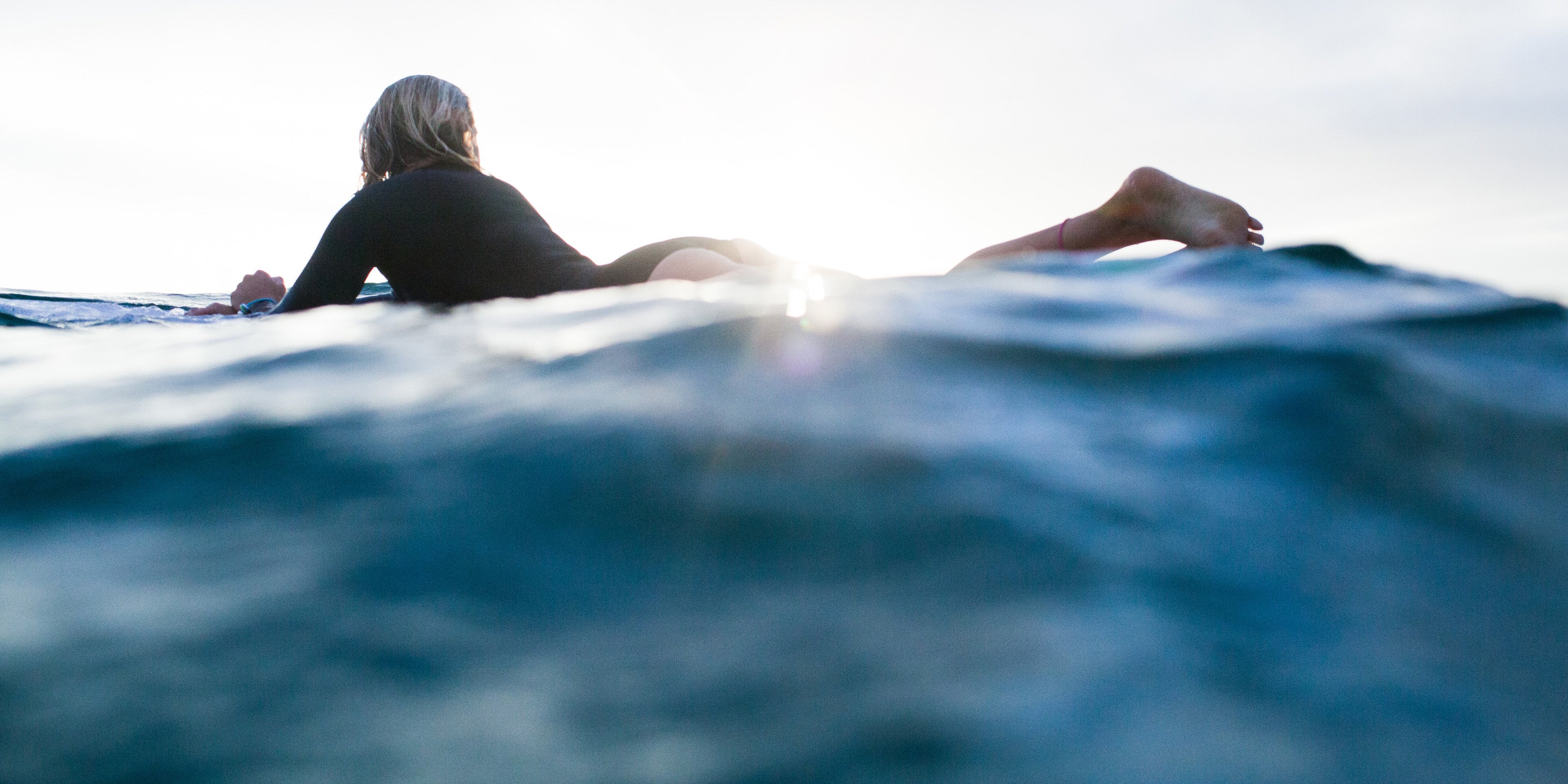 Woman on surfboard floating on the sea at sunset.