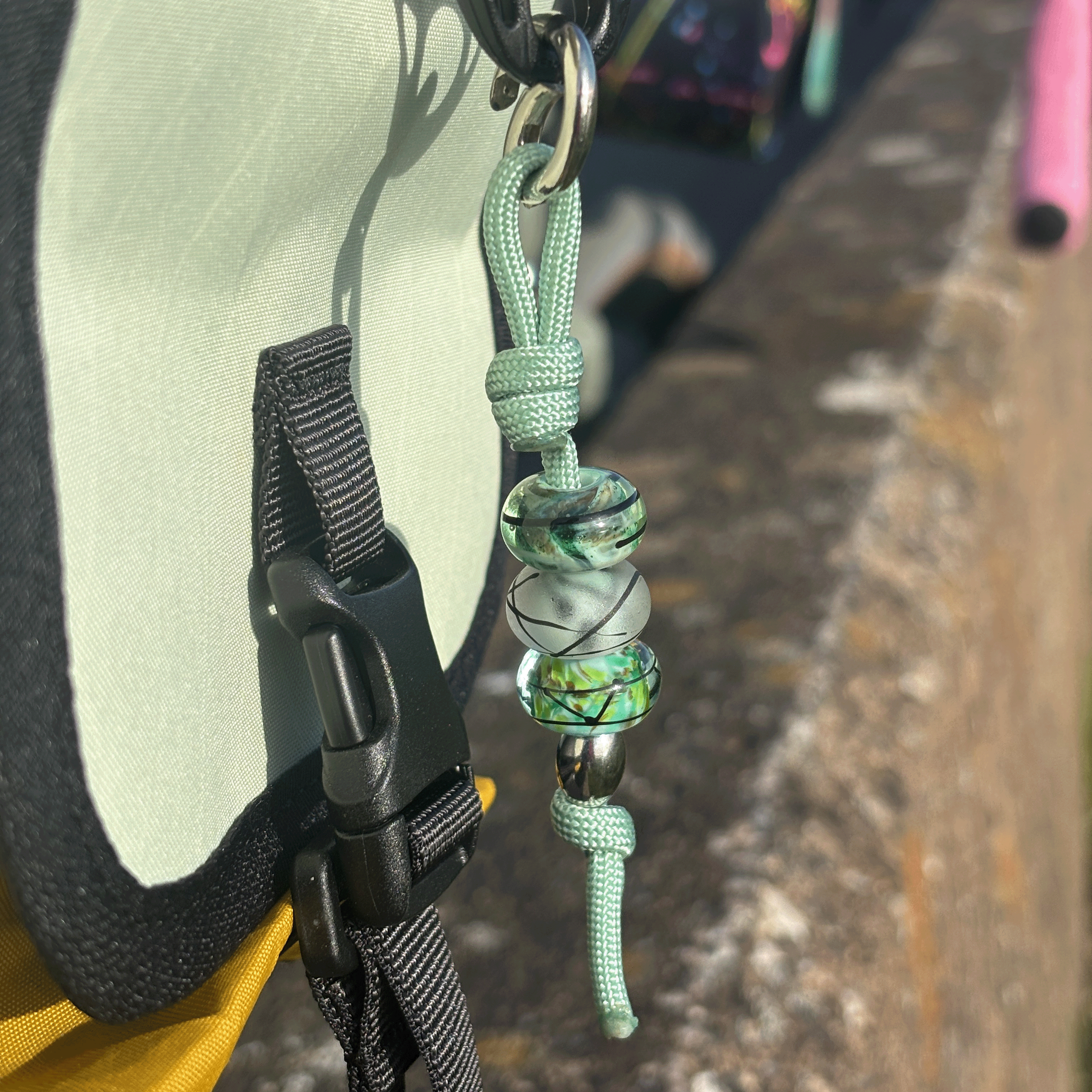 Green beaded keychain attached to a hat on a blurred outdoor background
