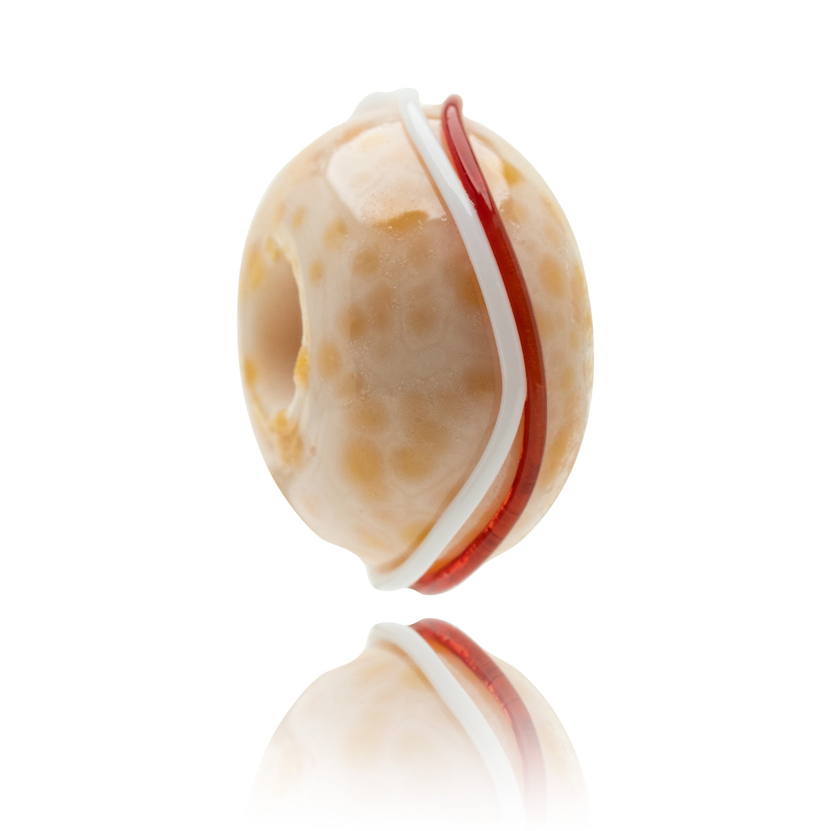 A single oval glass bead with a warm cream and orange-brown speckled pattern, featuring a white band and a red accent stripe, shown on a reflective white surface.