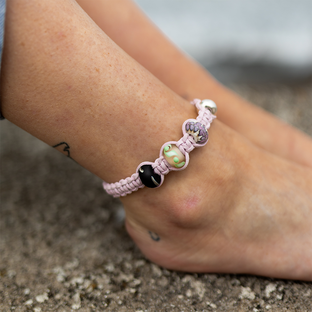 Person wearing thistle cord anklet with green, purple and Crean patterned glass beads.