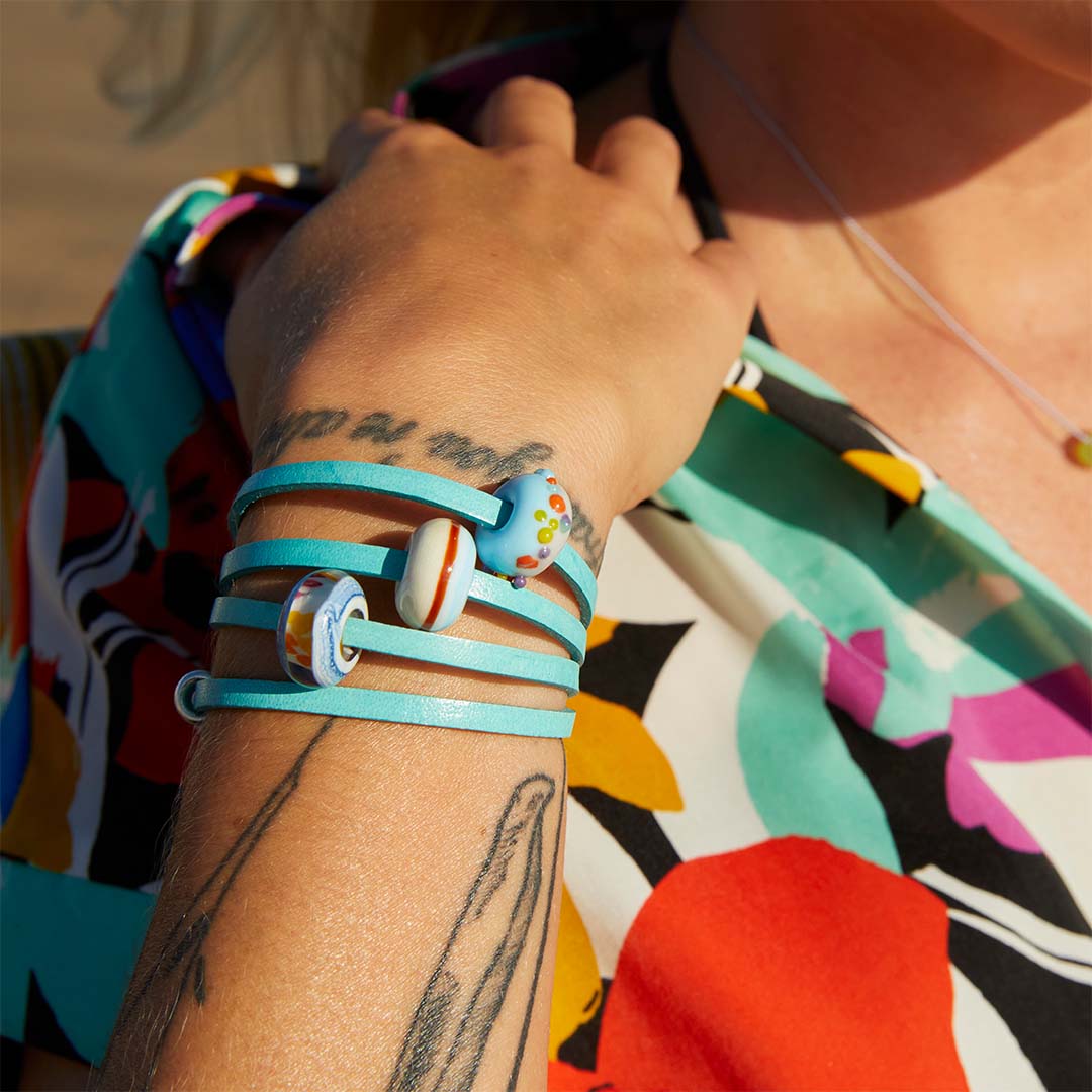 Woman in bright colourful shirt wearing a turquoise leather wrap bracelet with three colourful glass beads.