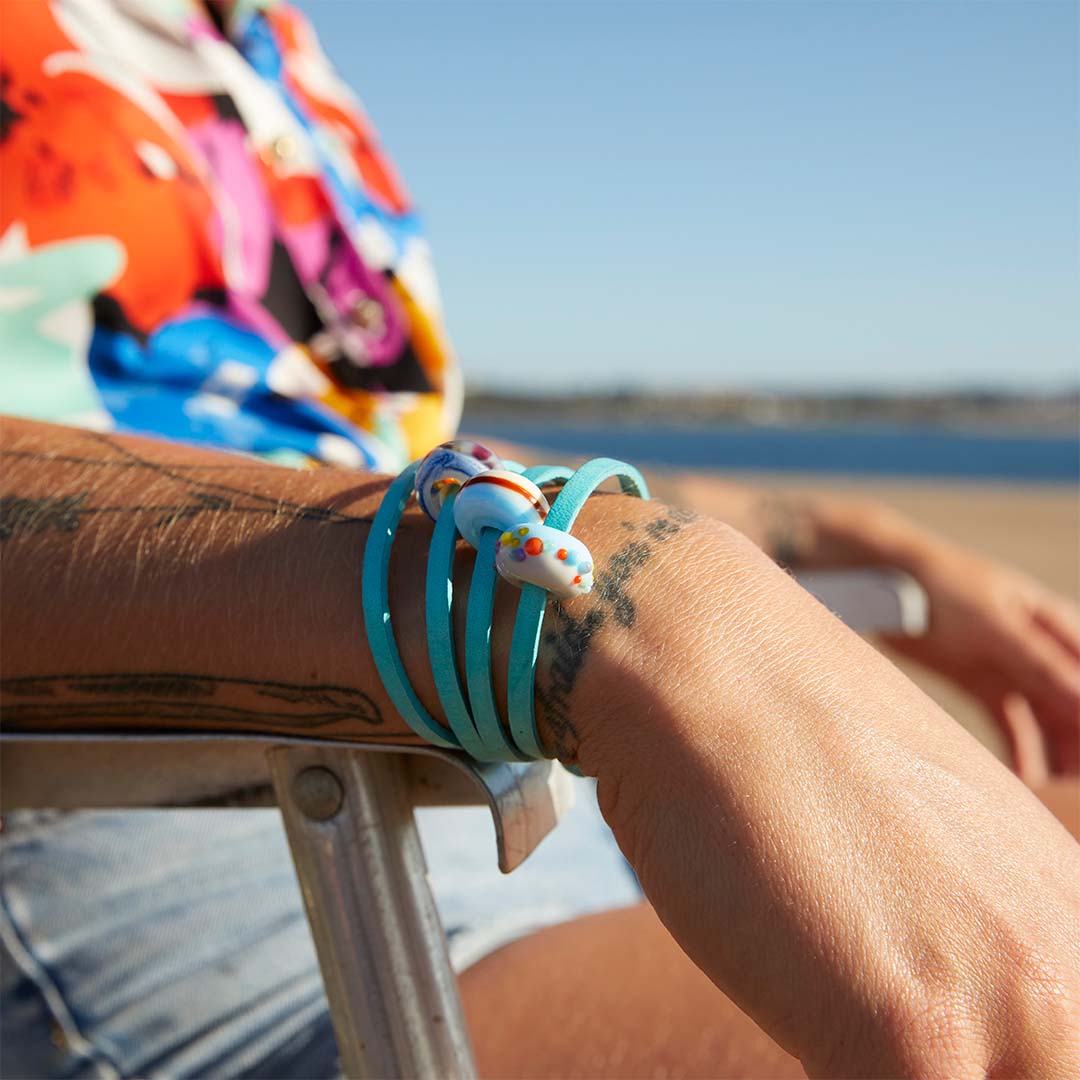 Woman in bright colourful shirt wearing a turquoise leather wrap bracelet with three colourful glass beads