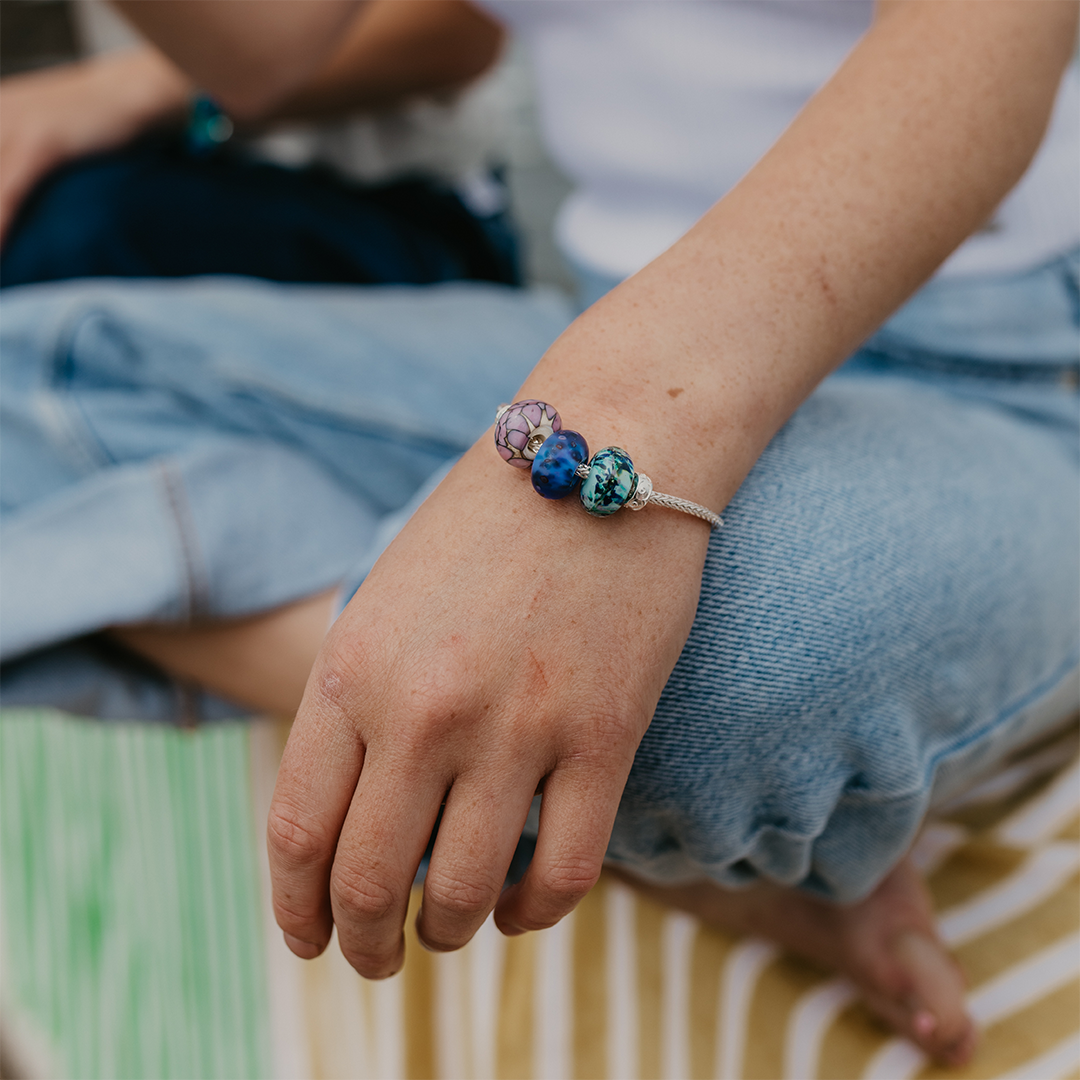 Person wearing jeans wearing a silver bracelet with patterned glass beads.