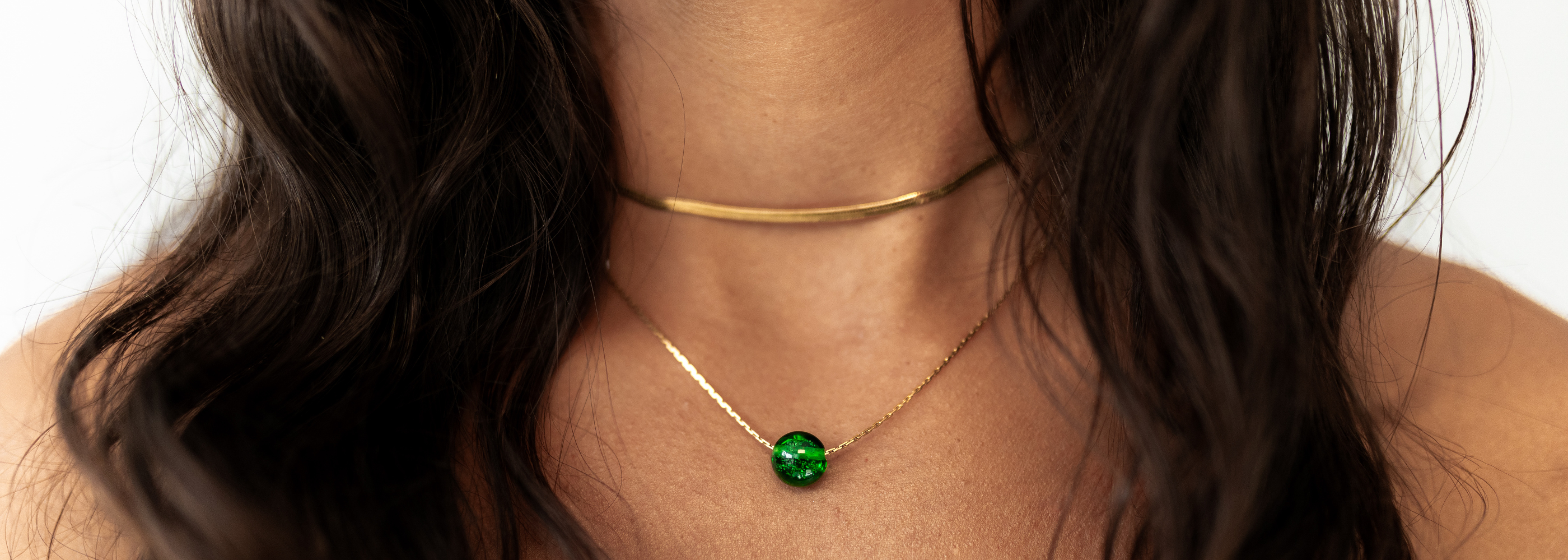Green glass bead on gold necklace worn by person wearing black.