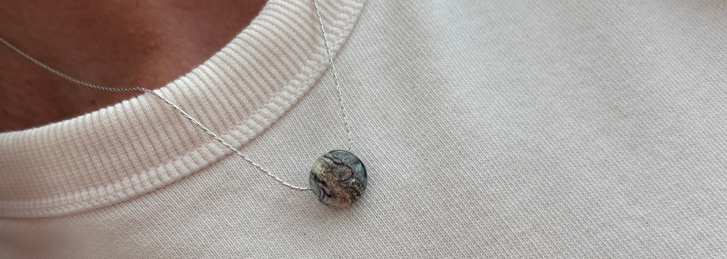 Mottled Grey glass pebble necklace worn by person in a white t-shirt.