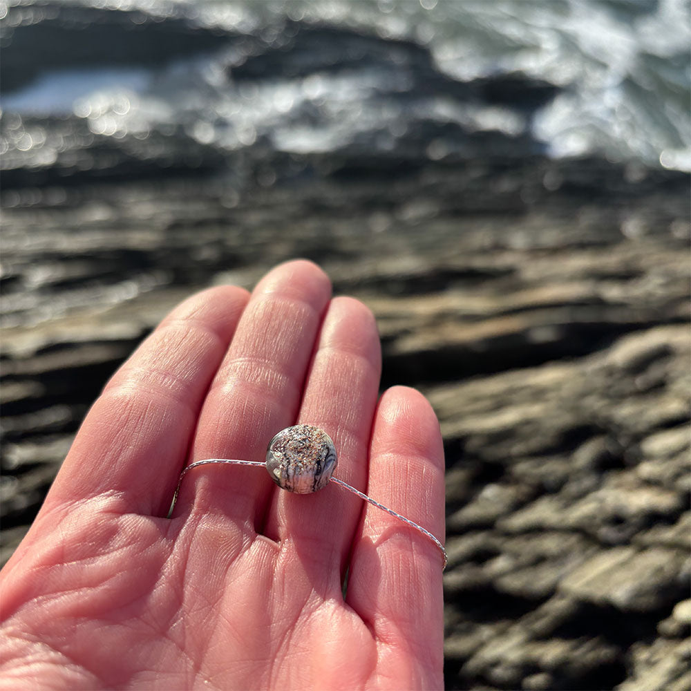 Hand holding a glass pebble pendant with sand texture ink the surface.