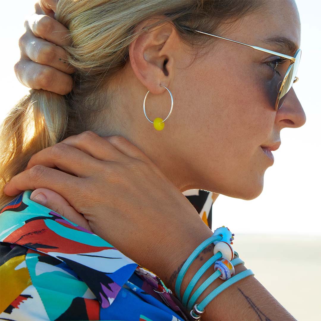 Woman in bright colourful shirt wearing a turquoise leather wrap bracelet with three colourful glass beads.