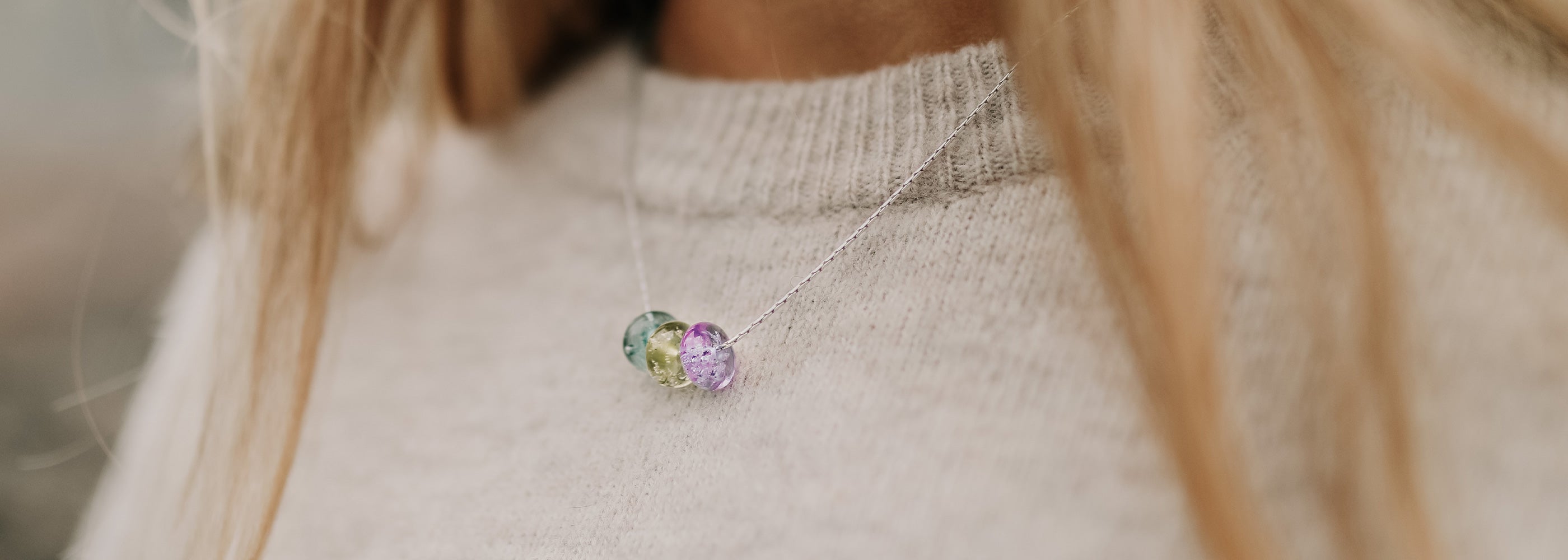 Green, purple and grey glass beads on sterling silver fine chain necklace worn by girl wearing a cream coloured sweater.