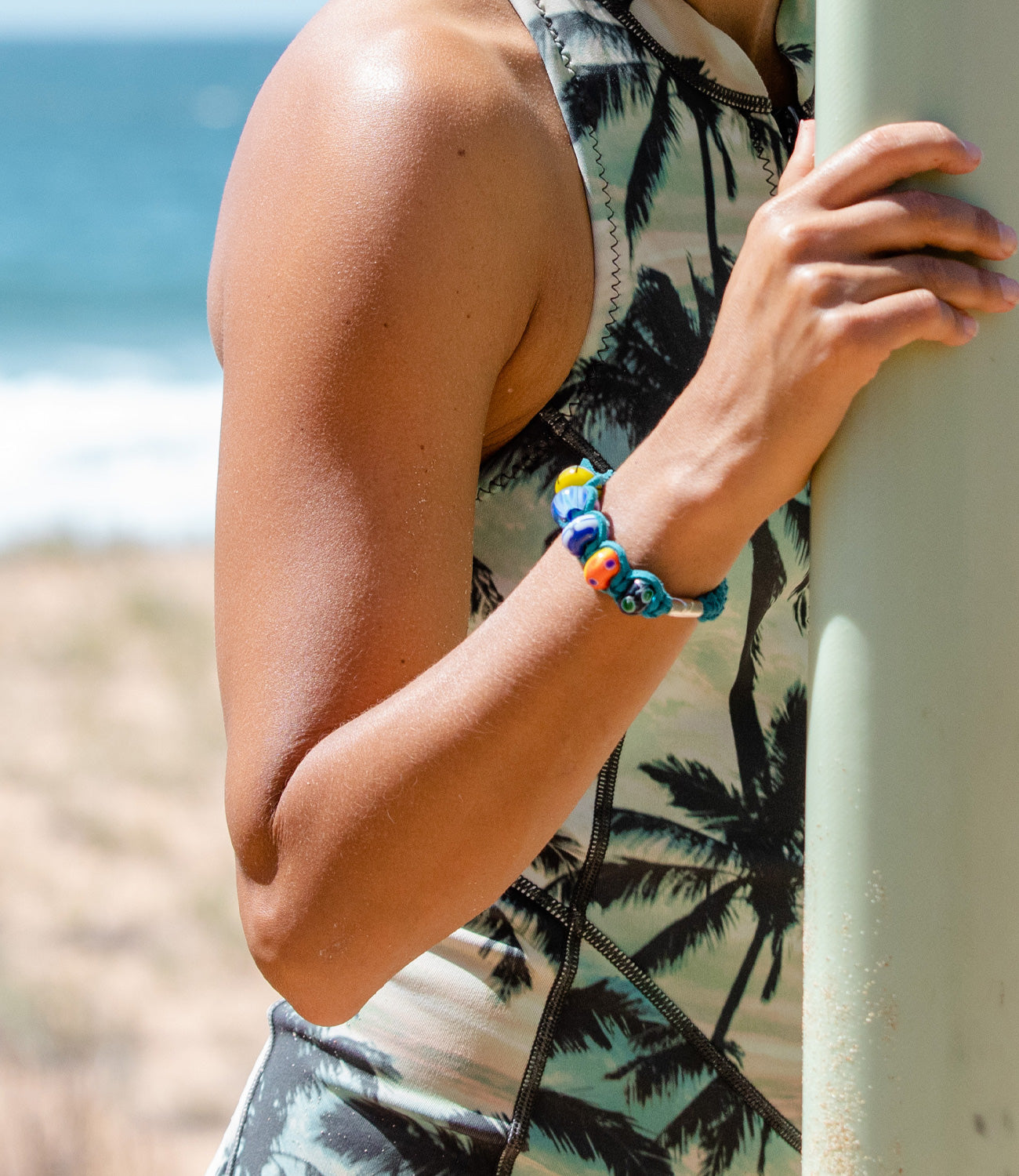 Custom macrame bracelet with colourful glass travel beads in teal cord, worn by surfer on the