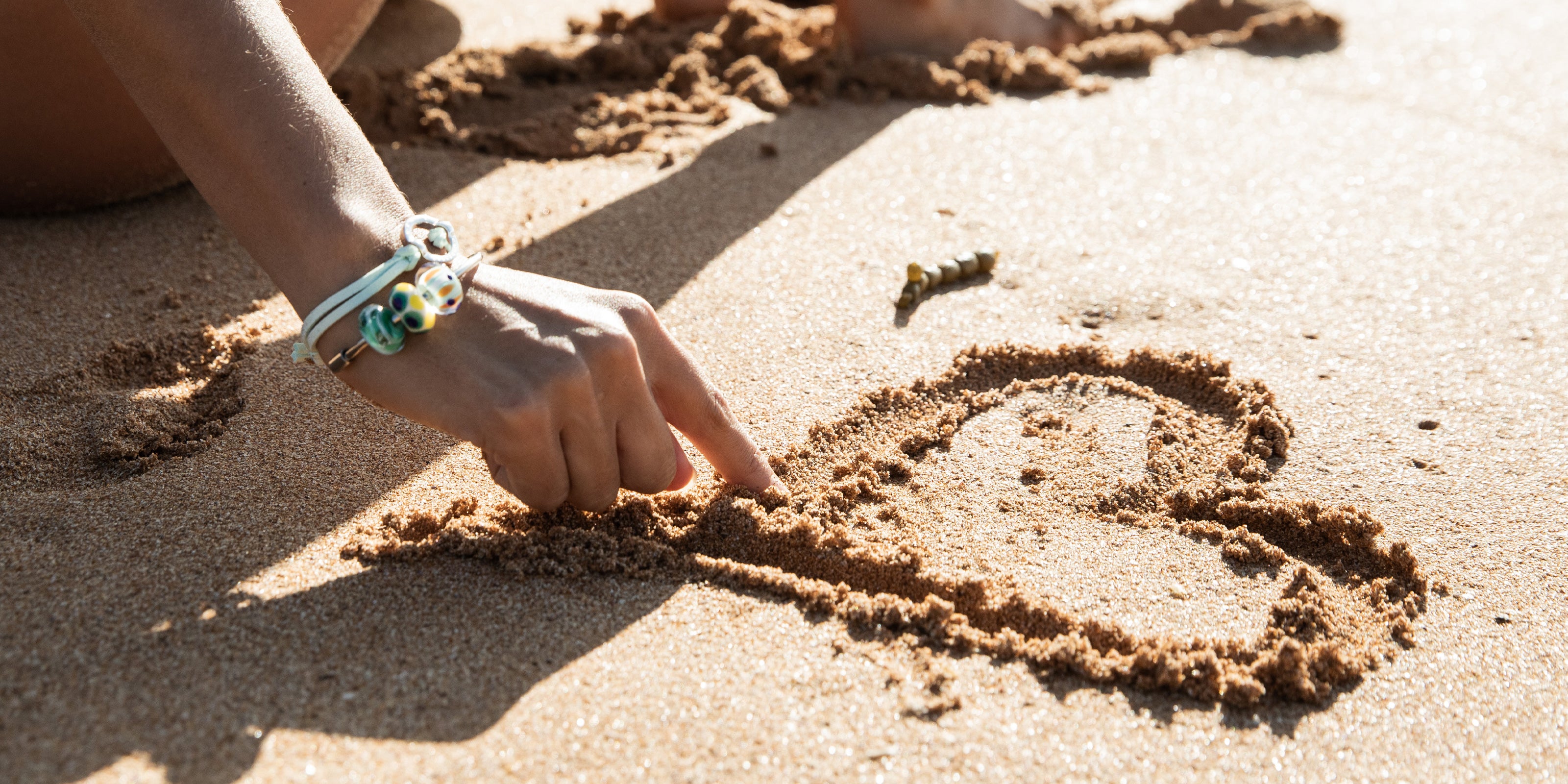 Drawing heart in the sand wearing colourful Nalu bracelet and bangle.