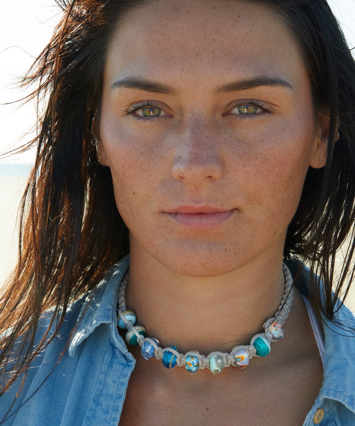 Grey macrame choker necklace made with colourful glass surf beads worn by woman in denim jacket.