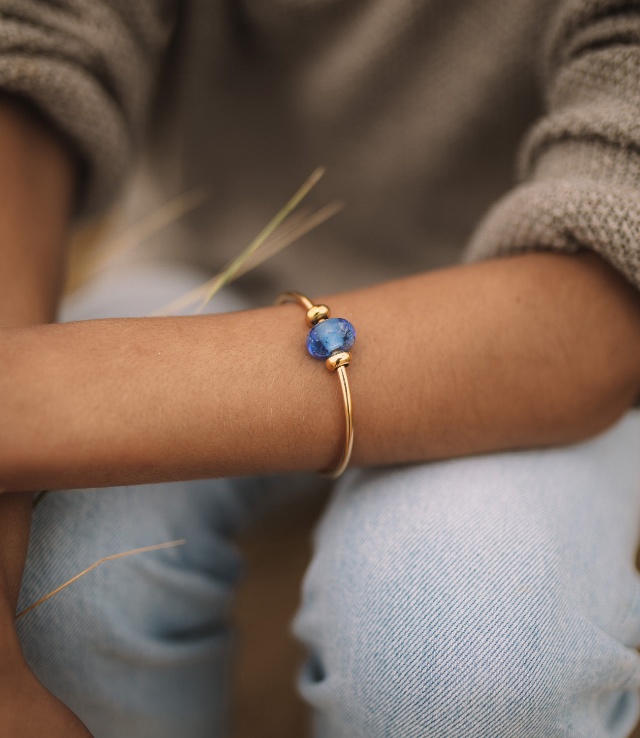 Gold bangle with dark blue sand bead worn by girl on beach.