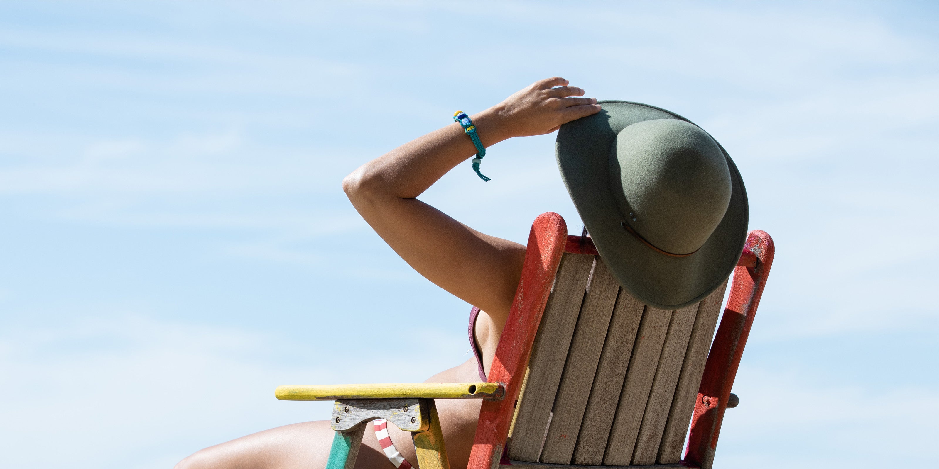 Woman on deckchair at the beach holding her hat wearing bracelet.