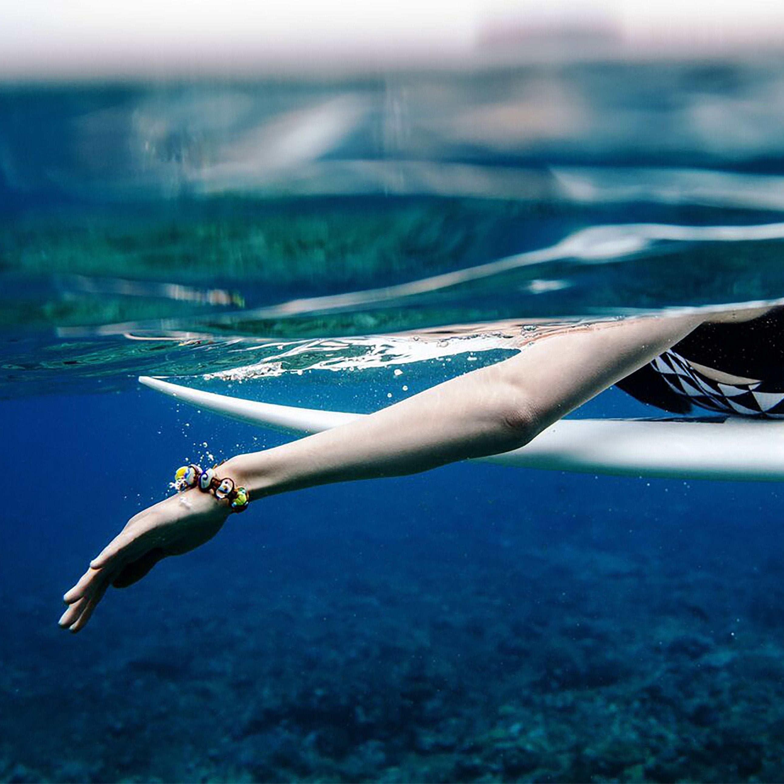 Surfer padding board through water wearing a bracelet.