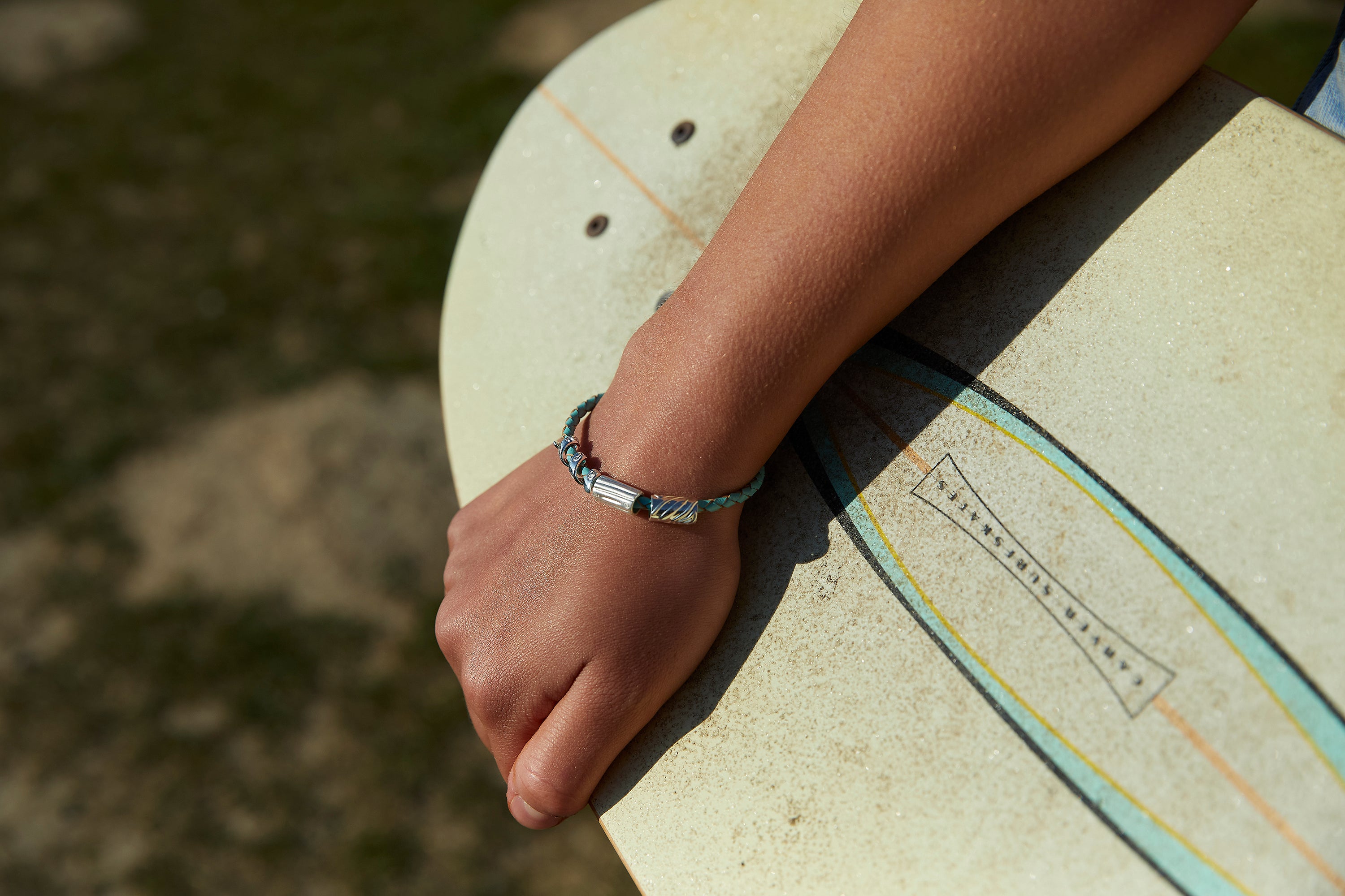 Silver charms inspired by the sea worn on a turquoise plaited bracelet.