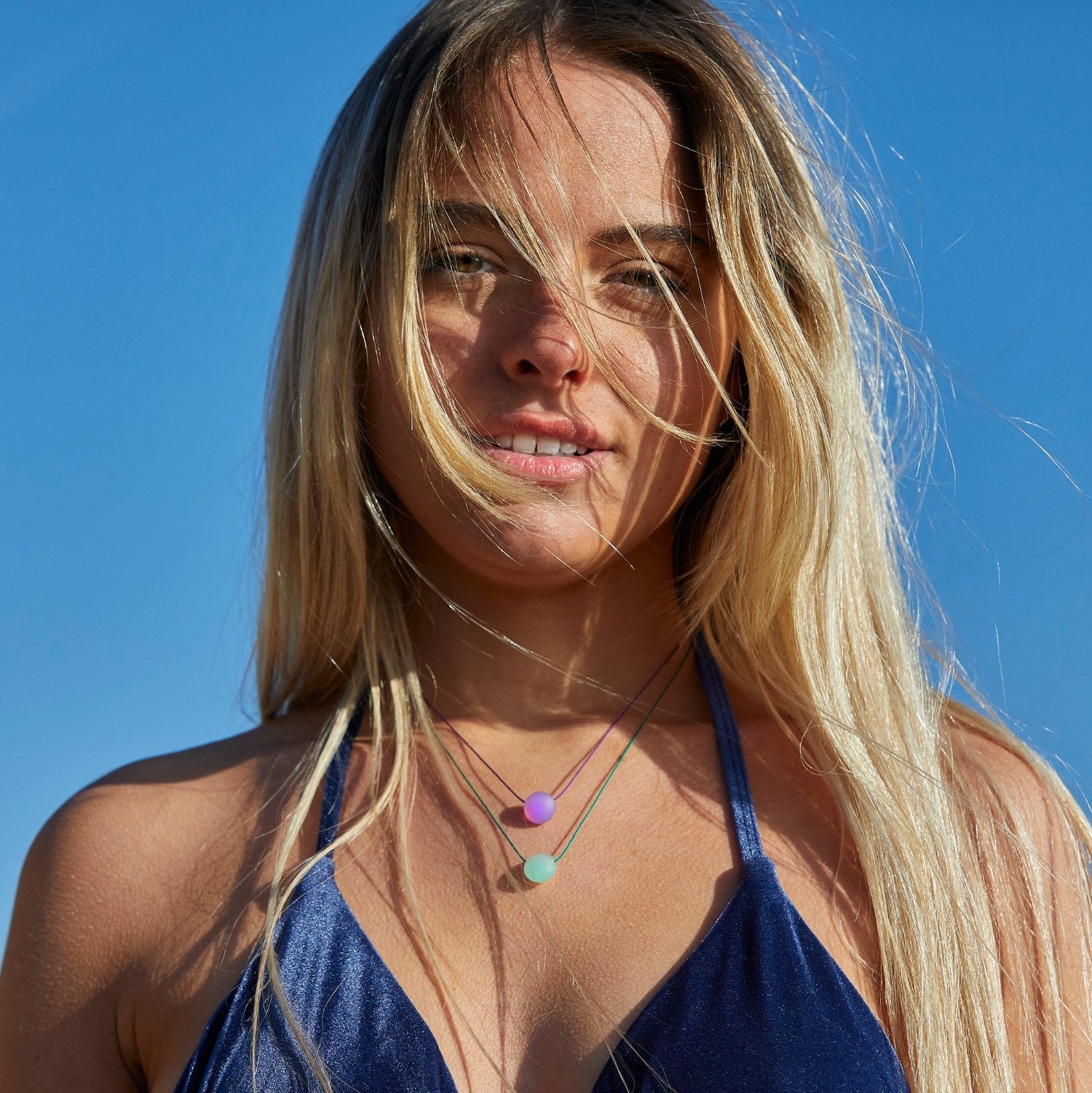 Blonde hair woman in velvet blue top, wearing purple and mint glass bead necklaces.