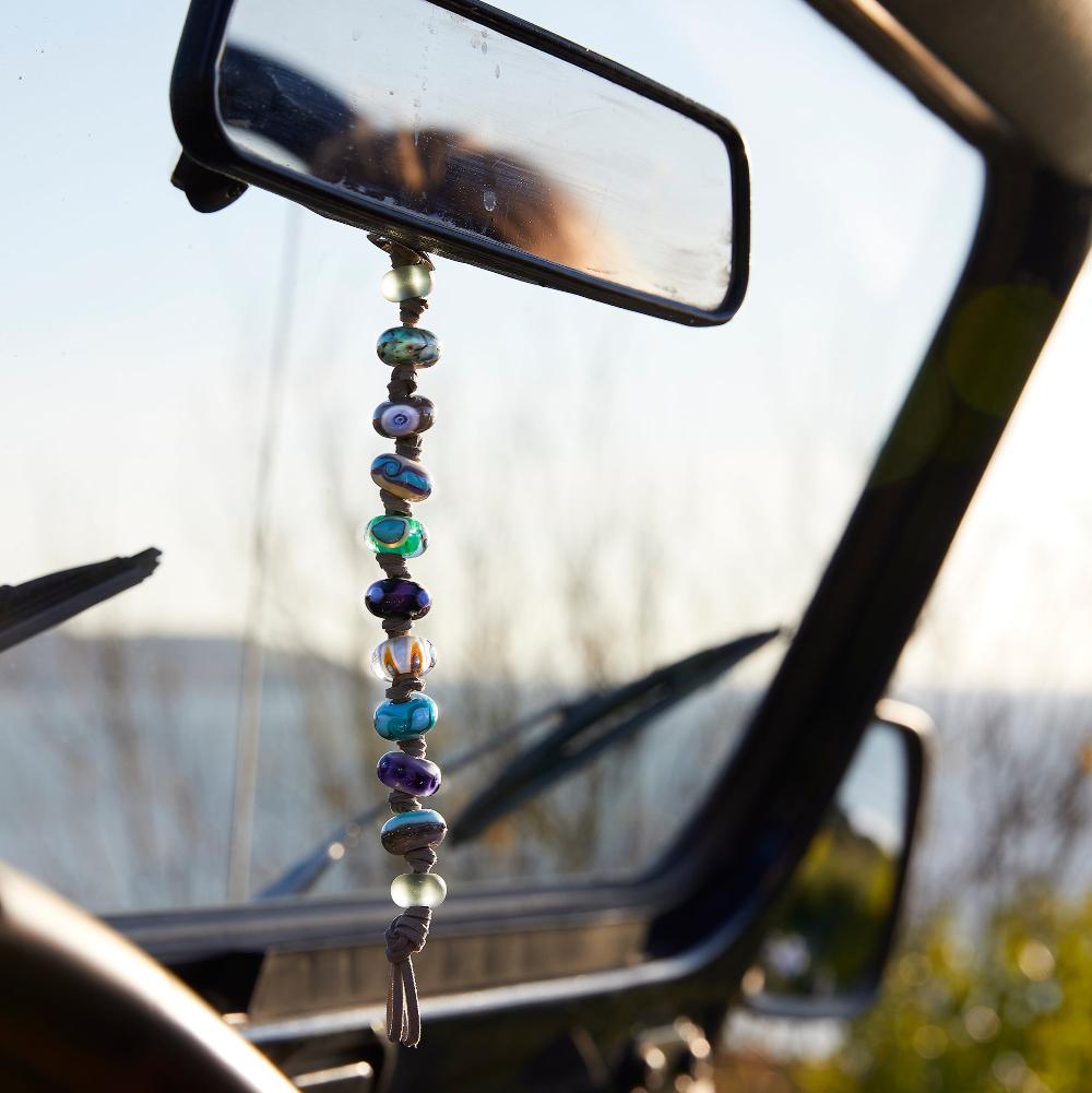 Beads hangin from rearview mirror in car parked next to beach.