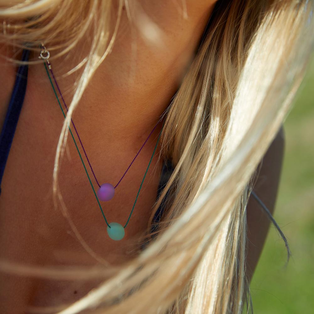 Woman wearing purple and green glass pebble necklace with blonde hair.