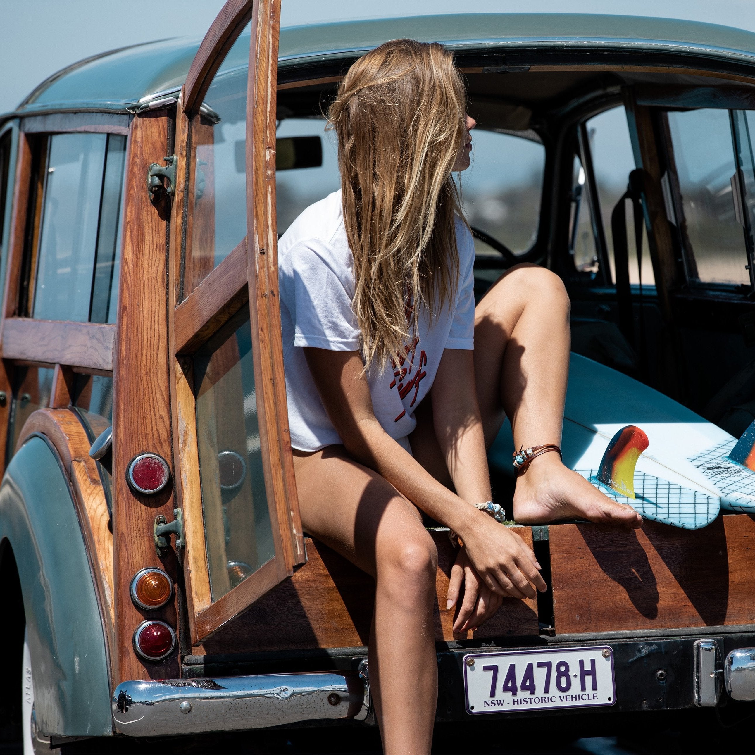 Woman with long hair sitting in the back of a car with her surfboard.