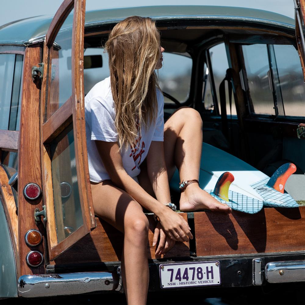 Woman sitting in back of a car with surfboards wearing Nalu Beads anklets and bracelets.